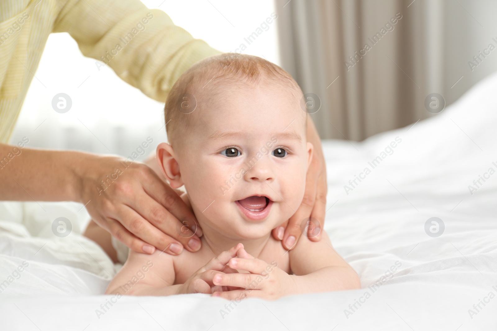 Photo of Young woman massaging cute little baby on bed indoors