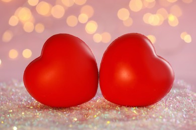 Photo of Red decorative hearts on glitter against blurred lights, closeup