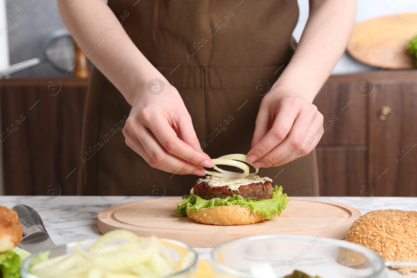 Photo of Woman making delicious vegetarian burger at white marble table, closeup