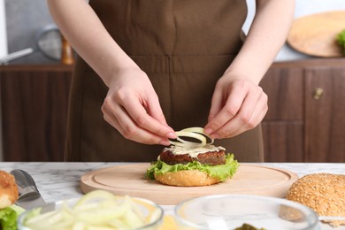 Photo of Woman making delicious vegetarian burger at white marble table, closeup