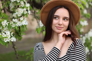 Photo of Beautiful woman in hat near blossoming tree on spring day