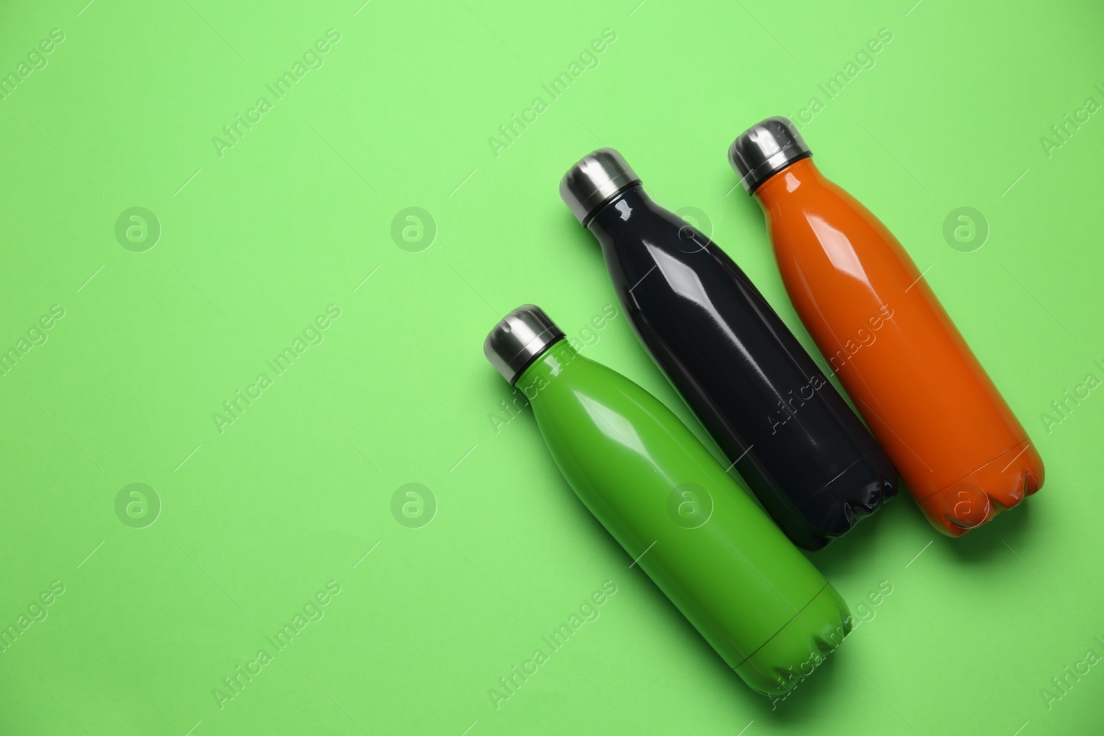 Photo of Different thermo bottles on green background, flat lay. Space for text