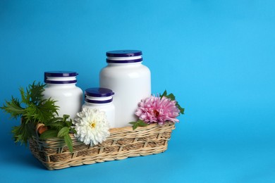 Photo of White medical bottles, arugula and flowers in wicker tray on light blue background, space for text