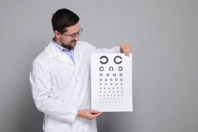 Photo of Ophthalmologist with vision test chart on gray background, space for text