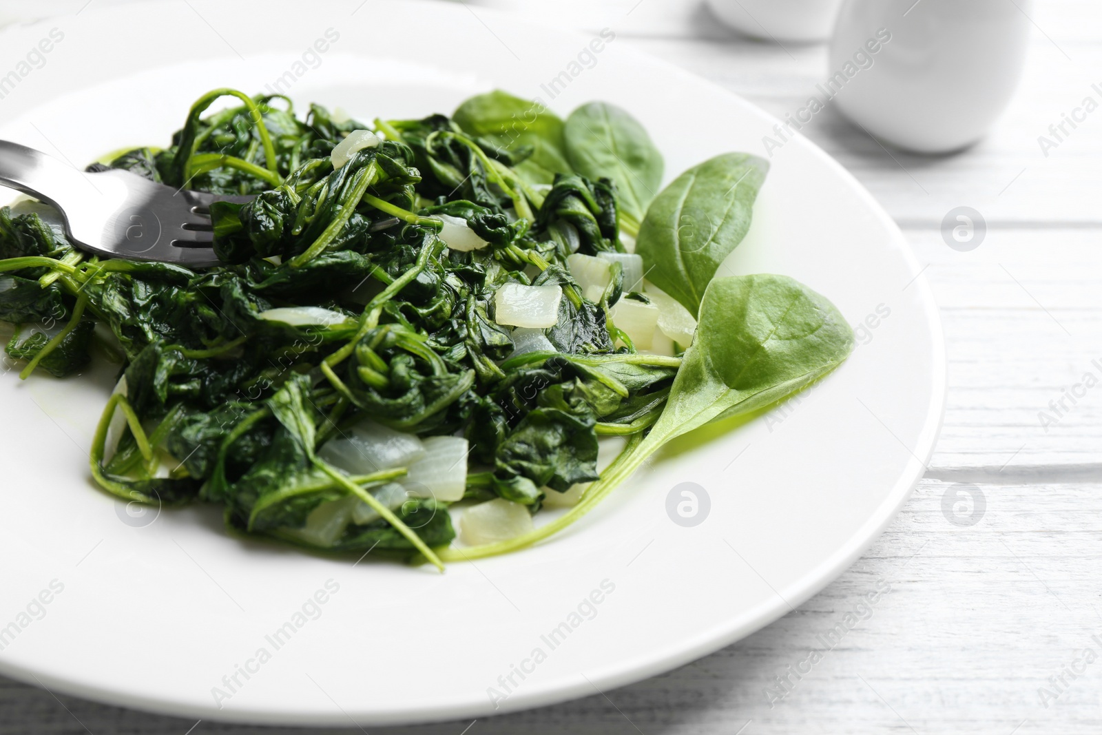 Photo of Tasty cooked spinach on white wooden table, closeup. Healthy food