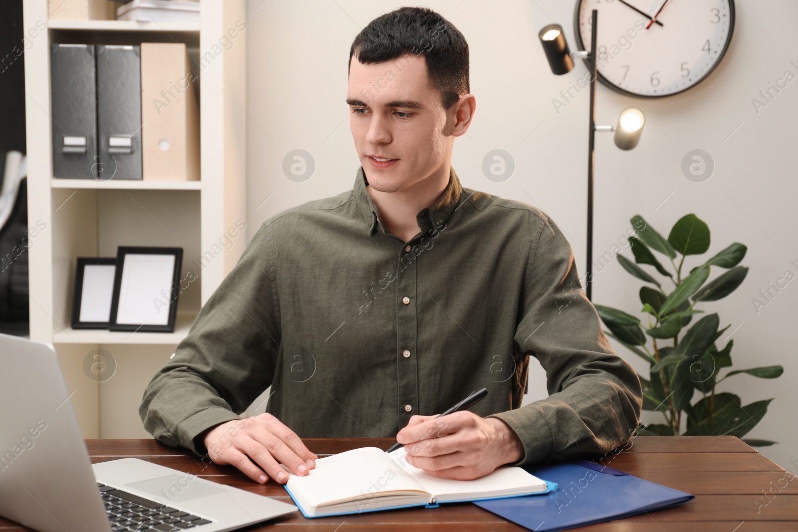 Photo of Man taking notes at wooden table in office