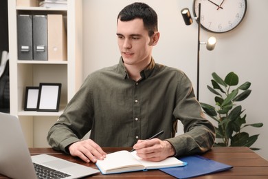 Photo of Man taking notes at wooden table in office