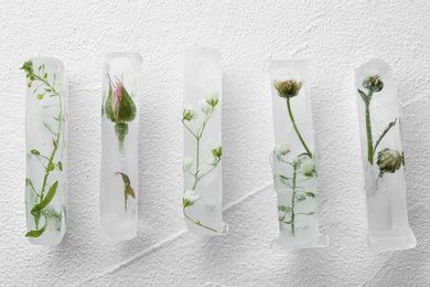 Photo of Ice cubes with flowers on white background, flat lay