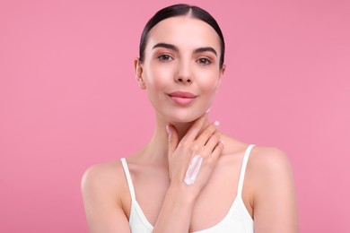 Photo of Beautiful woman with smear of body cream on her hand against pink background