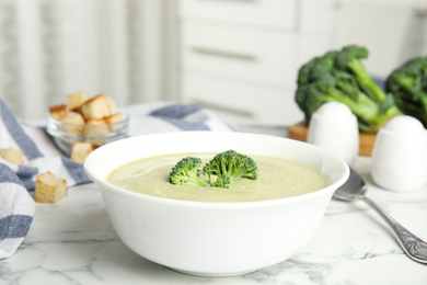 Photo of Delicious broccoli cream soup served on white marble table indoors