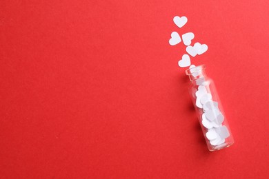 Photo of White paper hearts scattered from small glass bottle on red background, flat lay. Space for text