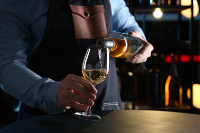 Bartender pouring white wine from bottle into glass at table indoors, closeup