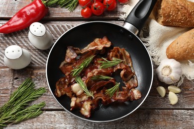 Delicious bacon slices in frying pan and products on wooden table, flat lay