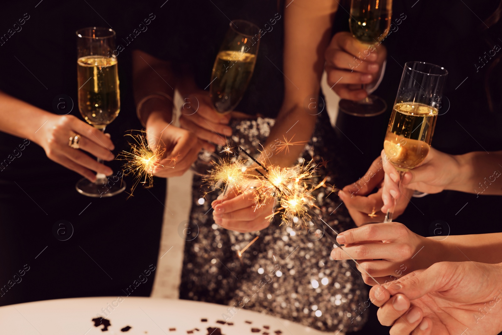 Photo of Friends with glasses of sparkling wine and sparklers celebrating New Year, closeup