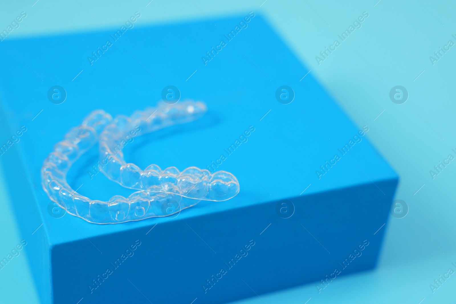 Photo of Transparent dental aligners on light blue background, closeup. Space for text