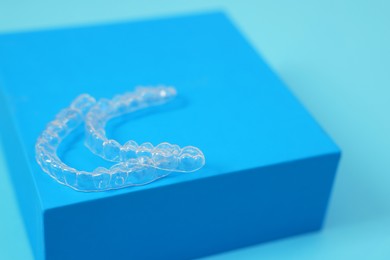 Transparent dental aligners on light blue background, closeup. Space for text