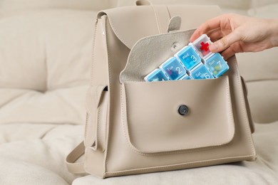 Photo of Woman putting pill box into backpack on sofa, closeup