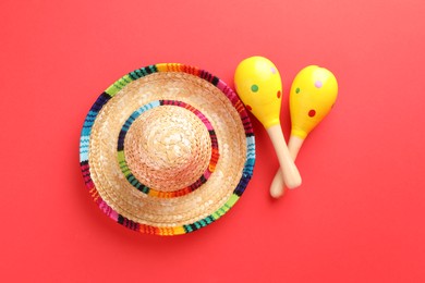 Photo of Mexican sombrero hat and maracas on red background, flat lay