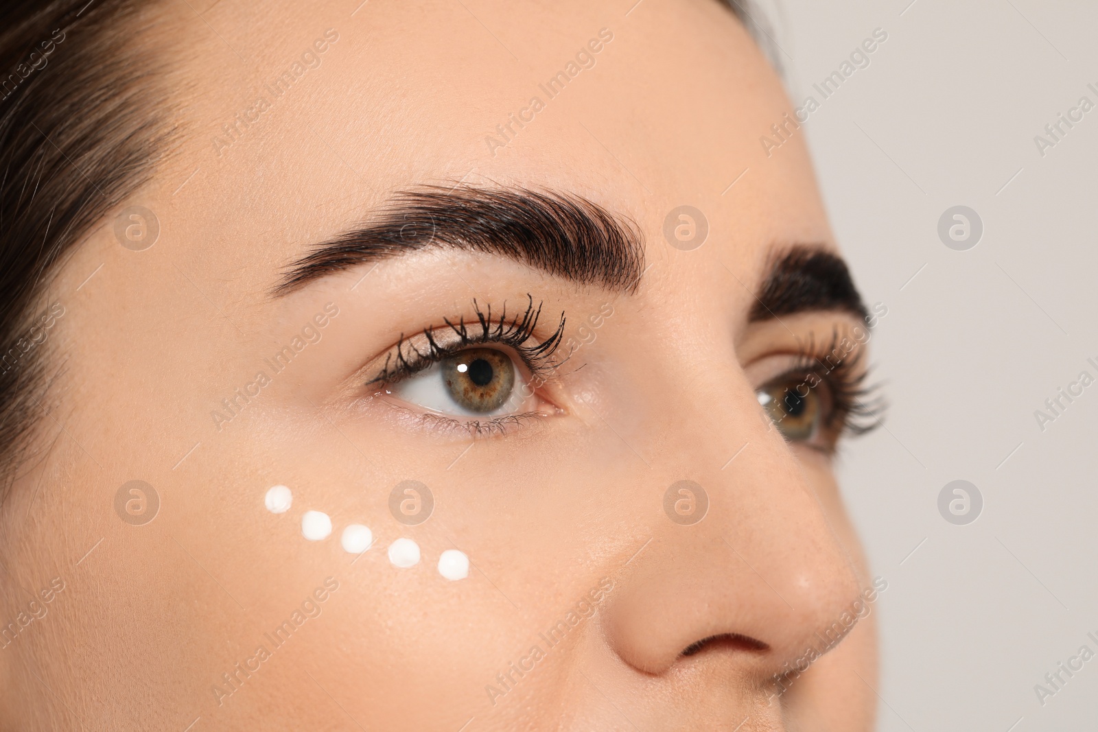 Photo of Woman with cosmetic product around eye on light background, closeup. Skin care