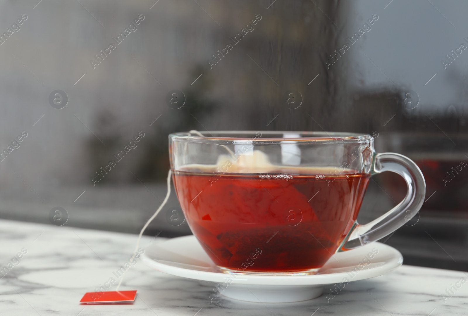 Photo of Glass cup of hot tea on window sill. Space for text