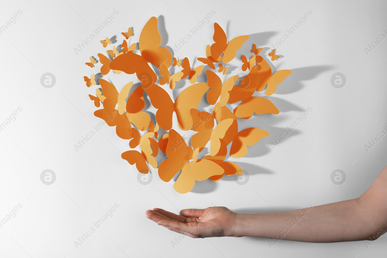 Image of Orange paper butterflies on white wall. Woman showing decorative element