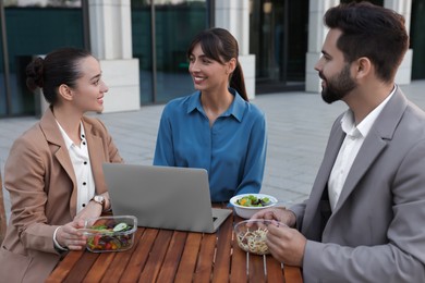 Business lunch. Happy colleagues with laptop spending time together at wooden table during break outdoors