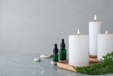 Photo of Burning candles and essential oil on grey marble table. Space for text