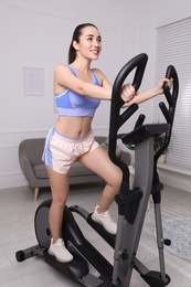 Photo of Happy young woman training on elliptical machine at home