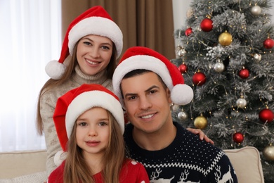 Happy family in Santa hats near Christmas tree at home