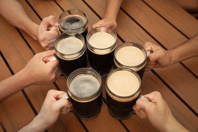 Photo of Friends clinking glasses with beer at table, closeup