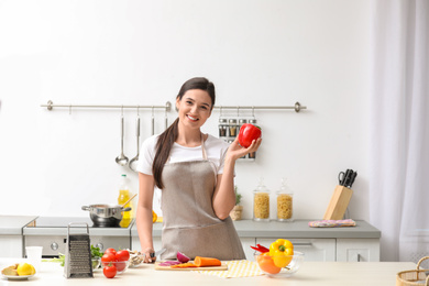 Photo of Young woman with bell pepper at table in kitchen. Cooking soup