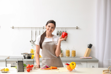 Young woman with bell pepper at table in kitchen. Cooking soup