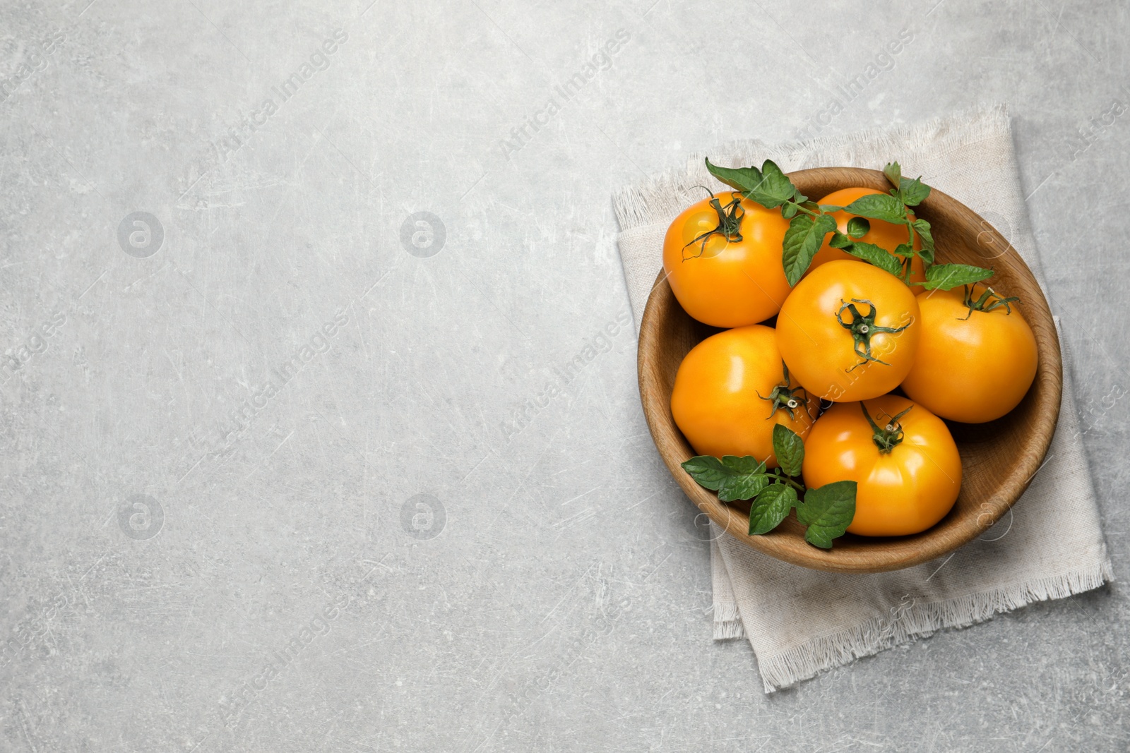 Photo of Fresh ripe yellow tomatoes with leaves on light grey table, top view. Space for text