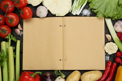 Blank recipe book surrounded by different ingredients on black wooden table, flat lay. Space for text