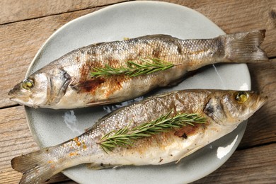 Photo of Delicious baked fish and rosemary on wooden table, top view