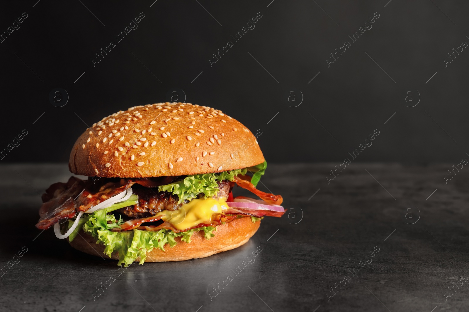 Photo of Tasty burger with bacon on dark background