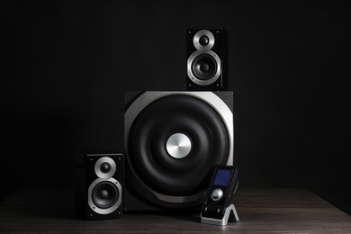Photo of Modern powerful audio speaker system with remote on wooden table against black background