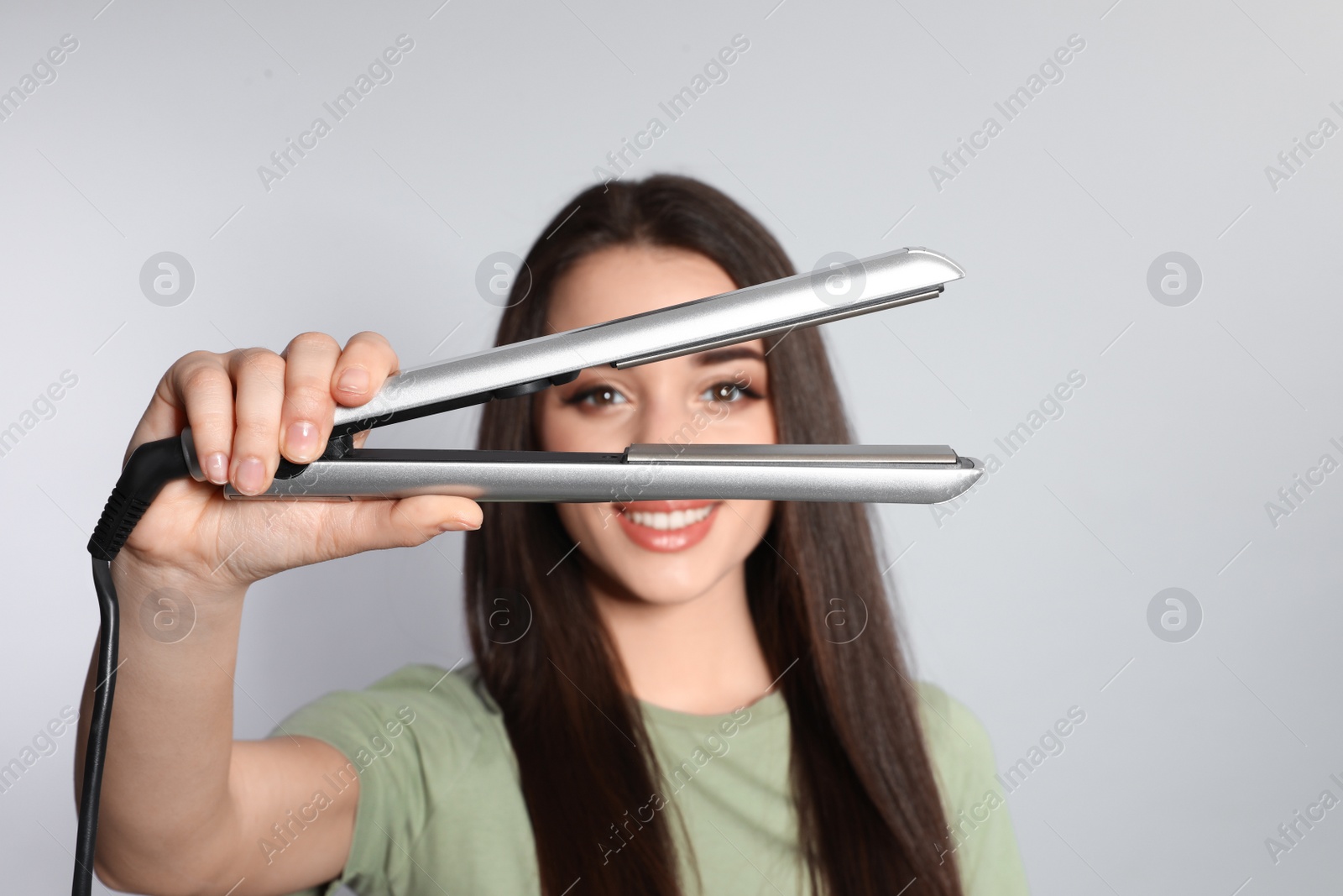 Photo of Happy woman with hair iron on grey background