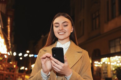 Photo of Smiling woman using smartphone on night city street