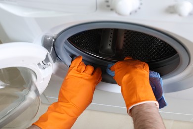 Photo of Man cleaning empty washing machine with rag, closeup