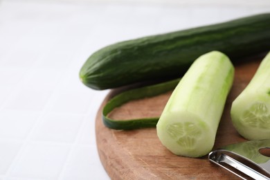 Fresh cucumbers and peeler on white tiled table, closeup. Space for text