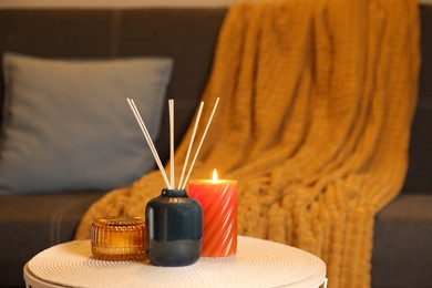 Aromatic reed air freshener and scented candles on wooden table indoors