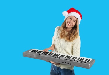 Young woman in Santa hat playing synthesizer on light blue background. Christmas music