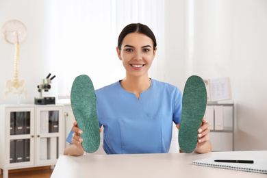 Young female orthopedist showing insoles in clinic