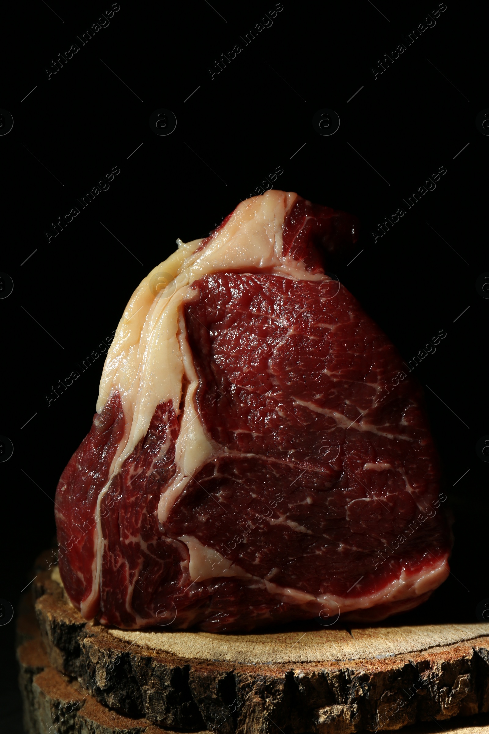 Photo of Piece of raw beef meat on decorative wooden stand against black background, closeup