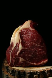 Piece of raw beef meat on decorative wooden stand against black background, closeup