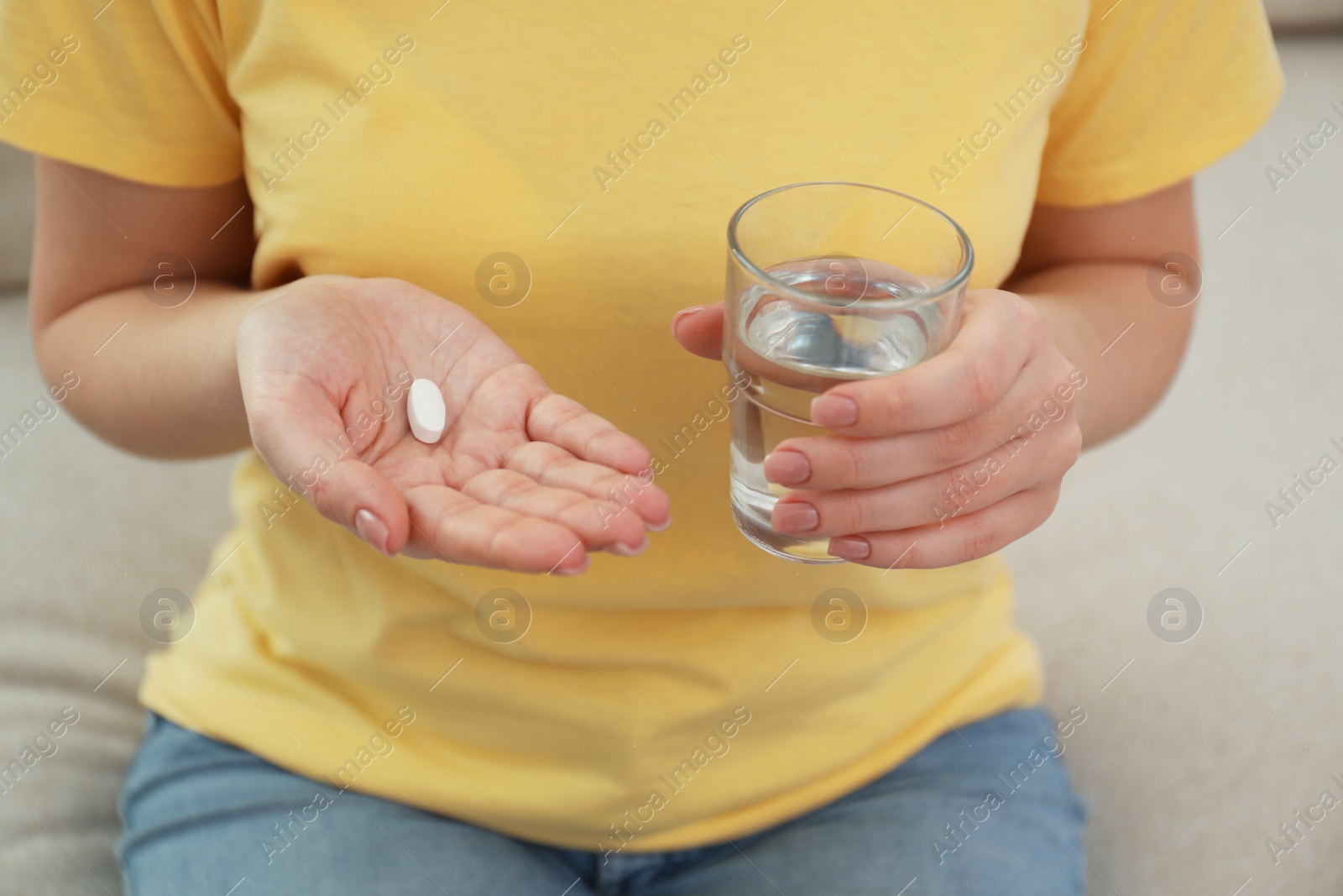 Photo of Young woman with abortion pill and glass of water on sofa, closeup