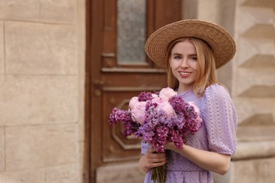 Photo of Beautiful woman with bouquet of spring flowers near building outdoors, space for text