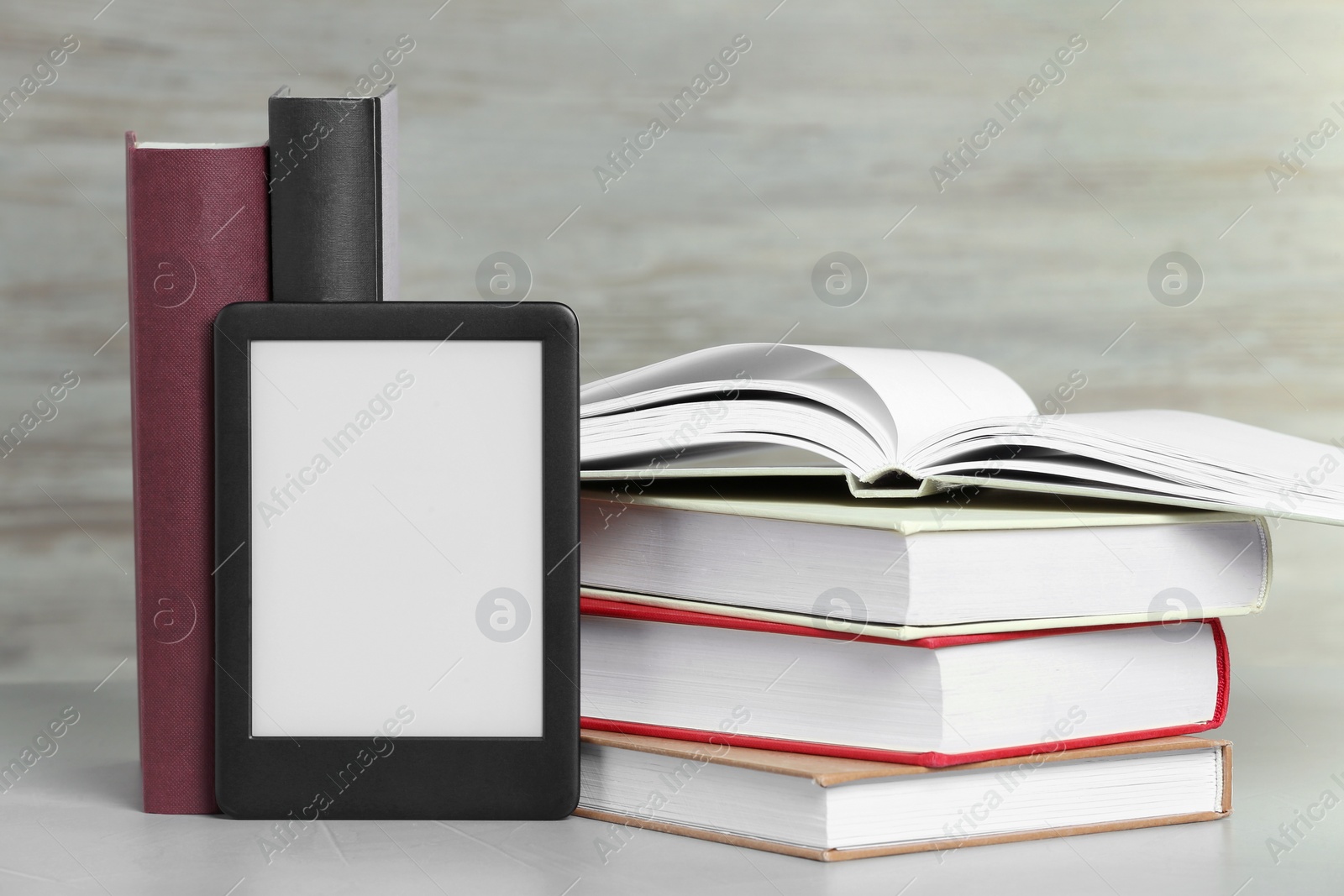 Photo of Portable e-book reader and many hardcover books on white textured table