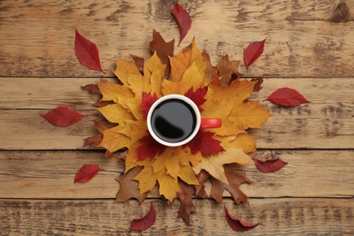 Cup of hot coffee and autumn leaves on wooden table, flat lay